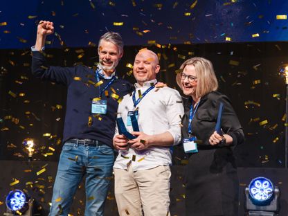 Flere som holder en pokal og jubler, på en scene. Konfetti og god stemning. 