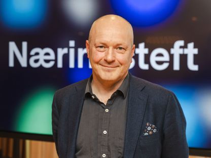 Mann uten hår, med dressjakke og skjorte ser i kamera. Skjerm med Næringsteft bak. 