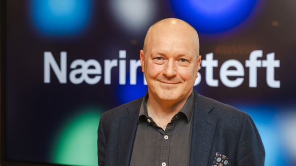 Mann uten hår, med dressjakke og skjorte ser i kamera. Skjerm med Næringsteft bak. 