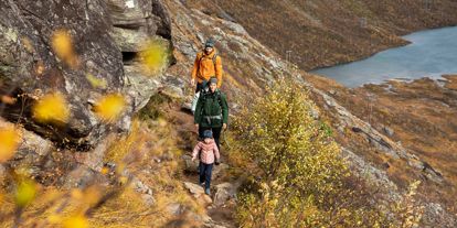 En liten familie med mor far og barn, som går på tur i høstfjellet. 