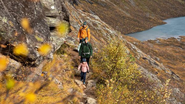 En liten familie med mor far og barn, som går på tur i høstfjellet. 