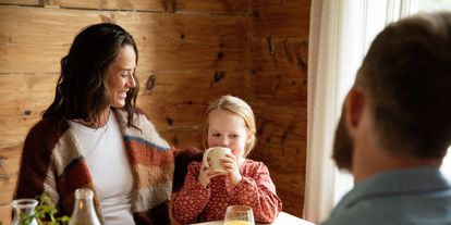 Familie som sitter rundt matbordet og smiler. 