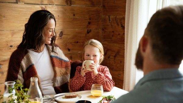 Familie som sitter rundt matbordet og smiler. 