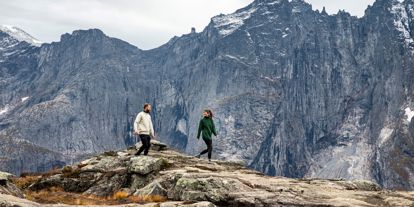 To personer som går på fjelltur - høye og taggete fjell i bakgrunnen