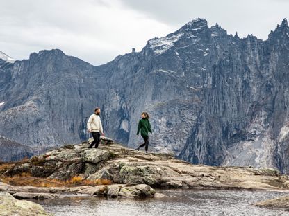To personer som går på fjelltur - høye og taggete fjell i bakgrunnen