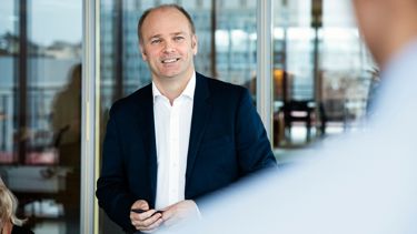 Mann med hvit skjorte og dressjakke, smiler 