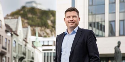 Mann i dress fremfor bygning i Ålesund. 