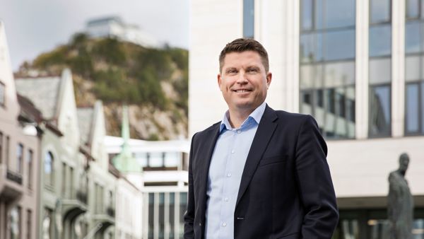 Mann i dress fremfor bygning i Ålesund. 