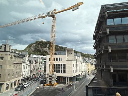 Sparebanken Møre sitt hovedkontor i Ålesund, med fjellstua i bakgrunn, og en stor kran i forkant. 