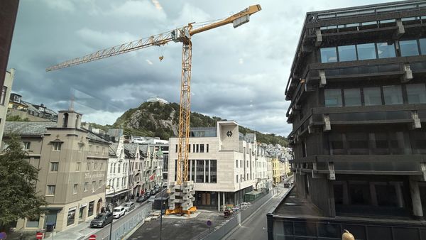 Sparebanken Møre sitt hovedkontor i Ålesund, med fjellstua i bakgrunn, og en stor kran i forkant. 
