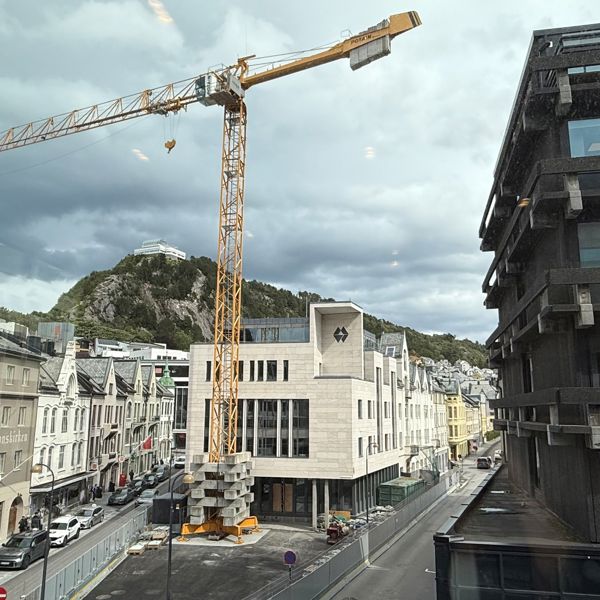 Sparebanken Møre sitt hovedkontor i Ålesund, med fjellstua i bakgrunn, og en stor kran i forkant. 