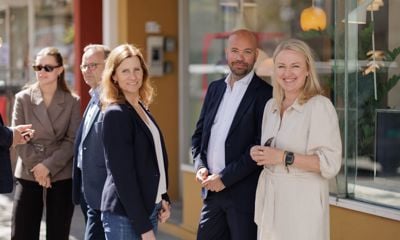 Bildet viser tre glade mennesker i solskinn i en handlegate som smiler mot kamera.