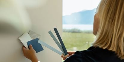 Dame som står med ryggen til og holder fargeprøver i blåtoner inn mot en lys vegg. 
