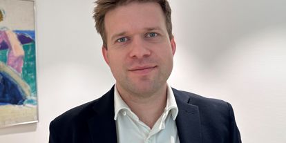 Mann i dress og hvit skjorte, ser i kamera. 