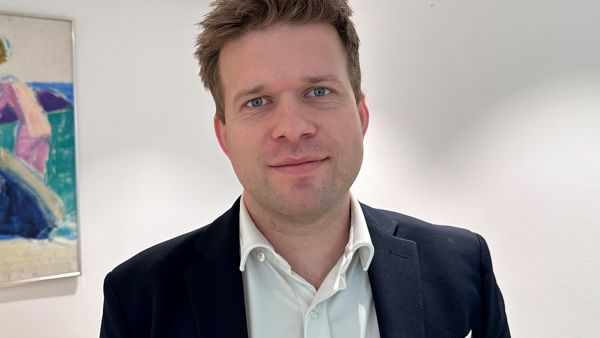 Mann i dress og hvit skjorte, ser i kamera. 