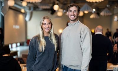 Kvinne med langt lyst hår og mann med kort hår, begge kledd i collegegenser, står sammen og smiler mot kamera. 