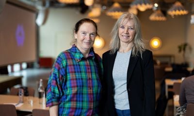 To kvinner som står sammen og ser i kamera. En kledd i t-skjorte og dressjakke, den andre i rutete skjorte. 
