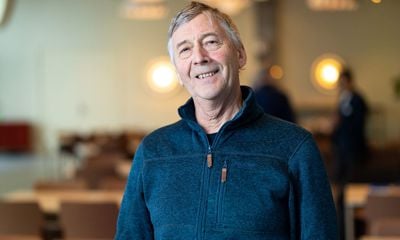 Mann med grått hår, blå fleecejakke. Smiler og ser i kamera. Blurret bakgrunn. 