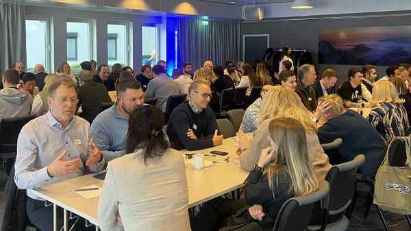 Forsamling med mennesker som sitter på langbord i et kurslokale - i samtale med hverandre