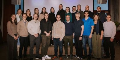 To oppstilte rekker med mennesker, kvinner og menn, står foran et lerret i et arrangementslokale.