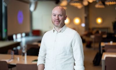 Mann med kvit skjorte, smiler til kamera - blurret bakgrunn. 