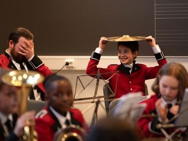 Korpsmusikanter. En musikant holder en symbal på hodet. En annen musikant holder hendene foran ansiktet. 