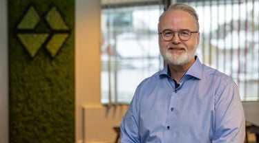 Mann med blå skjorte, briller og skjegg smiler til kamera
