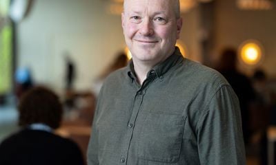 Mann med mørk grønn skjorte, smiler og ser i kamera. Blurret bakgrunn. 