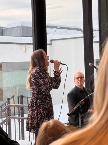Dame sett fra siden som holder en mikrofon og synger. Mann i bakgrunnen. 