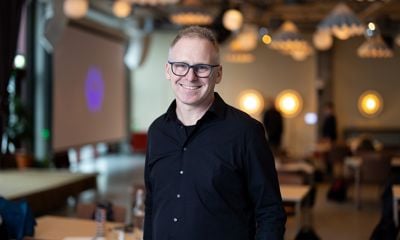 Mann med mørk skjorte og briller. Smiler til kamera - blurret bakgrunn. 