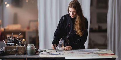 Ung kvinne arbeider med å håndkolorere et grafisk trykk i sitt atelier.