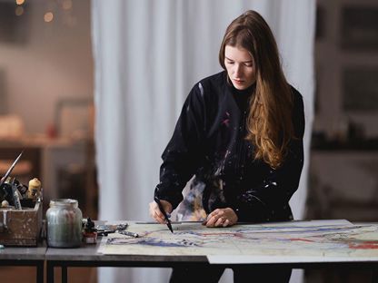 Ung kvinne arbeider med å håndkolorere et grafisk trykk i sitt atelier.