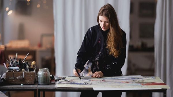 Ung kvinne arbeider med å håndkolorere et grafisk trykk i sitt atelier.