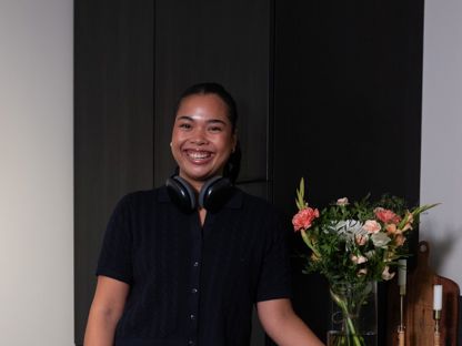 Ung kvinne med headset rundt halsen, på kjøkkenet. Hun står oppreist og smiler til kamera