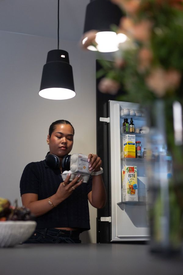Ung kvinne som er ut av vinduet med kaffi i hånden, moderne leilighet i by. 