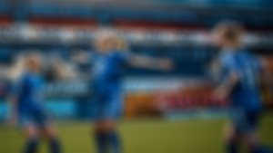 Tre glade fotballjenter i blå drakt på stadion.